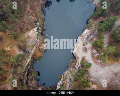 Picturesque aerial view of landscape with emerald lake and rocks in the middle of a coniferous autumn forest in Korostyshiv granite quarry, Zhytomyr d Stock Photo