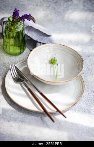 High angle of autumnal table setting with ceramic bowl and plate with flower near fork, knife, napkin and vase with lavender flowers against gray surf Stock Photo