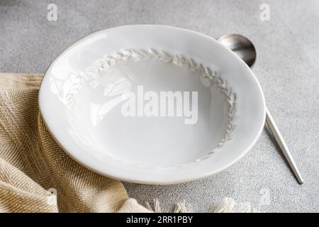 High angle of autumnal table setting with white ceramic bowl between spoon and napkin against gray surface Stock Photo