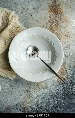 Top view of autumnal table setting with white ceramic bowl and spoon on napkin against gray surface Stock Photo