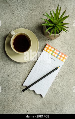 Top view of mug of coffee near potted plant and note with pencil placed on gray table Stock Photo