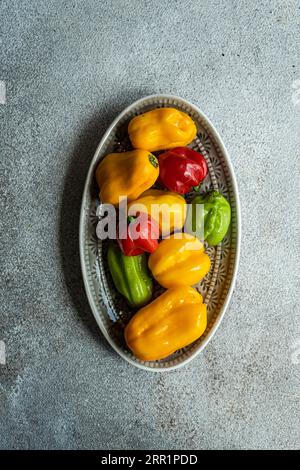 Top view of different colored peppers placed on a ceramic platter on a concrete background Stock Photo