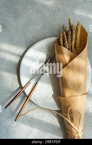 Top view of summer table setting with plate, knife, fork and wheat placed on gray table Stock Photo