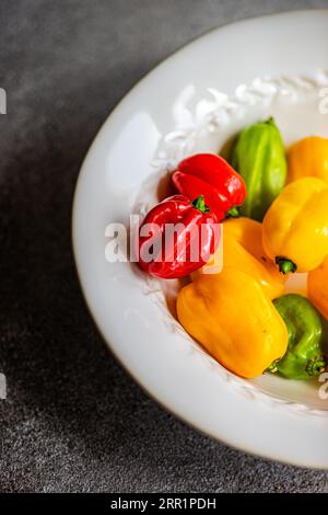 Top view of different colored peppers placed in a round white ceramic plate on a concrete background Stock Photo
