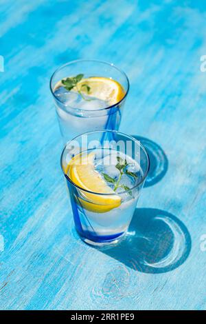 High angle of Summer cocktails with lemon vodka, slices of lemon and wild mint leaves served with ice placed on blue table Stock Photo