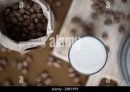 Top view of home made organic horchata drink served in a modern transparent glass near bottle of blurred almonds in a rustic kitchen Stock Photo