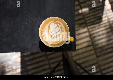 Top view of ceramic mug with fresh aromatic creamy latte coffee placed on black dinning table in daylight Stock Photo