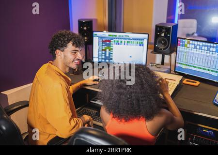 Male audio engineer and female African American vocalist enjoying recorded song in control room with computer sound software and mixing board Stock Photo