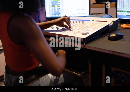 Crop anonymous African American female audio engineer creating music and using mixing board and sound software in control room Stock Photo
