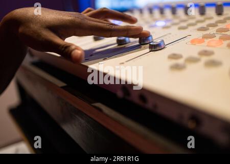 Crop anonymous African American female audio engineer creating music and using mixing board and sound software in control room Stock Photo