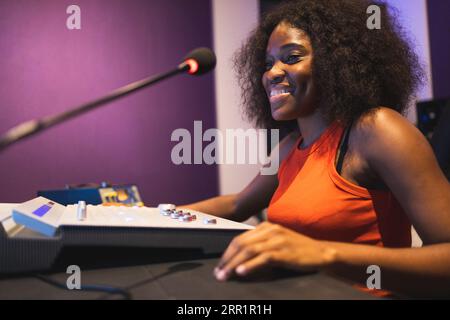 Cheerful African American female audio engineer working in music recording studio and using mixing board and software for creating modern song Stock Photo