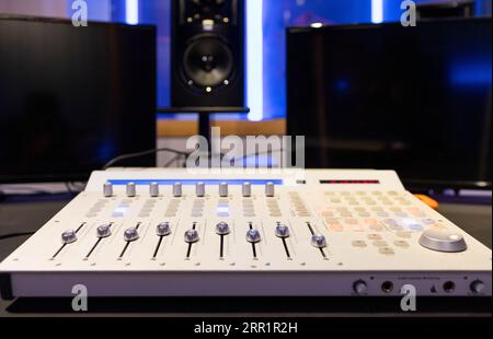 Mixing digital audio workstation controller with knobs channel strip display bus compressor plug ins placed in studio lights against blurred wall Stock Photo