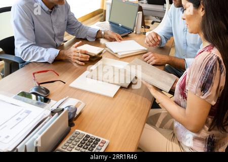 High angle of clients with material samples of facades of kitchen cabinets and discussing details with interior designer in office of furniture store Stock Photo