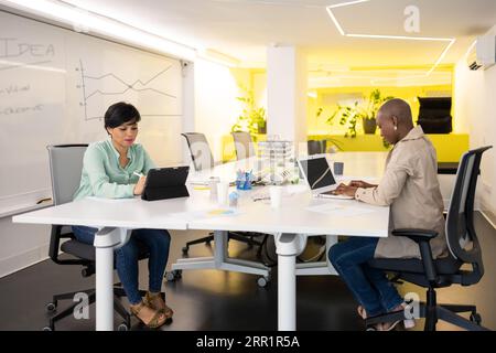 Concentrated multiracial female colleagues sitting at desk in modern office and working on project together using laptop and tablet Stock Photo