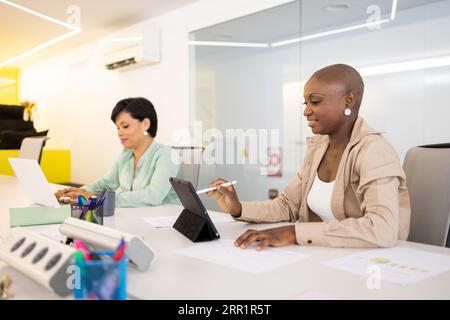 Diverse colleagues working on project together using laptop and tablet while sitting at white desk in modern office Stock Photo