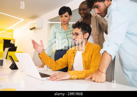 Group of multiracial coworkers gathering together at table and working on project using laptop in modern office Stock Photo