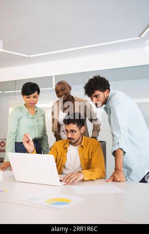 Group of multiracial coworkers gathering together at table and working on project using laptop in modern office Stock Photo