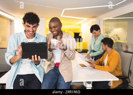 Cheerful multiracial male and female using tablet while colleagues working on laptop together in modern office Stock Photo