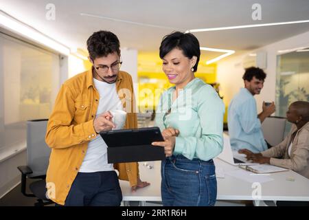 Cheerful male and female using tablet while colleagues multiracial working on laptop together in modern office Stock Photo