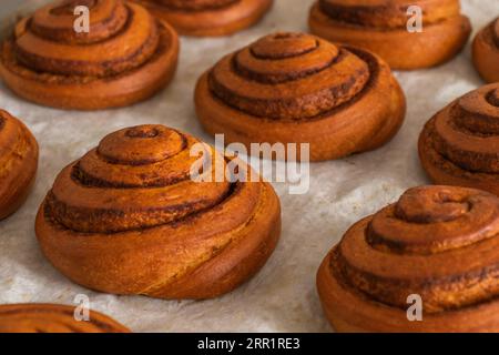 Closeup of freshly baked collection of crispy delicious cinnamon rolls on bright marble table in bakery Stock Photo