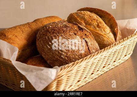 Various tasty freshly baked pastry breads being served with baking pan into wicker basket with fabric on dining table indoors Stock Photo
