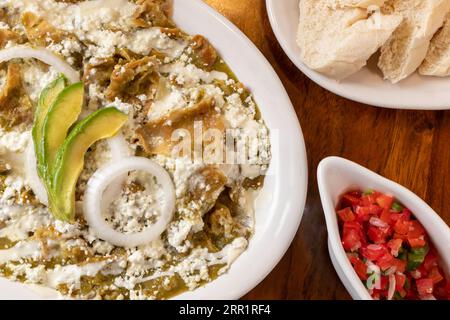 Top view of delicious Pico de Gallo salad in bowl chilaquiles with avocado onions corn tortillas served on white plate along with raw cheese on wooden Stock Photo