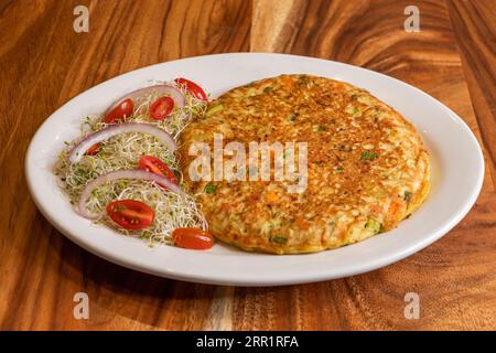From above of yummy omelette prepared with chopped onions potatoes eggs coriander leaves while served on white plate along with sprouts garnished with Stock Photo