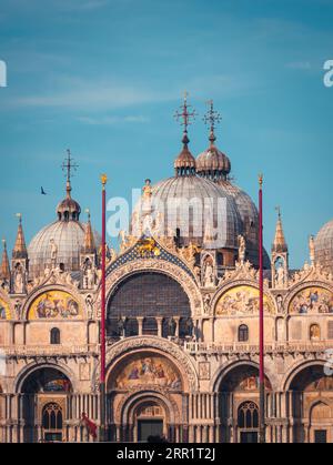 Ornamental facade of historic St Marks Basilica with arcades and domed roofs against bright blue sky in Venice Stock Photo