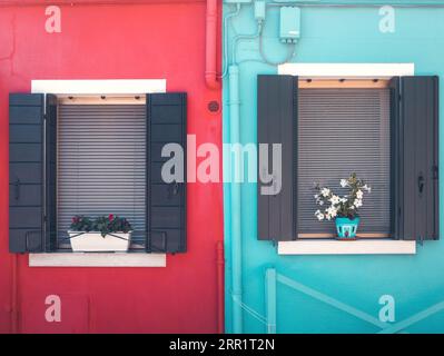 Exterior of blue and red dwelling homes with opened doors of netted windows with flowering plants in vases on sills located on clean marble street in Stock Photo
