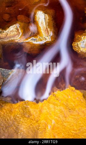 Top view of yellow marble stone with gold splashes and flowing fluid through cracks on shiny orange granular mineral formation in Mines of Rio Tinto H Stock Photo