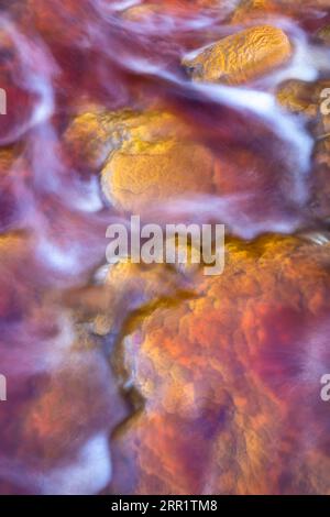 Top view of abstract background of orange and yellow colors stone with flowing violet fluid lines and micro granular minerals against blurred blue bac Stock Photo