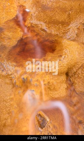 Top view of yellow marble stone with gold splashes and flowing fluid through cracks on shiny orange granular mineral formation in Mines of Rio Tinto H Stock Photo