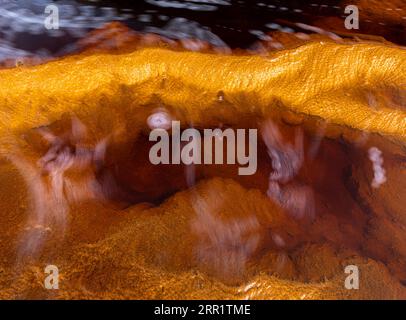 Top view of abstract background of orange and yellow colors stone with flowing violet fluid lines and micro granular minerals against blurred blue bac Stock Photo