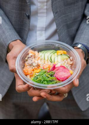 From above of anonymous male in formal dress while sitting in daylight showing healthy salad in bowl with fish and vegetables Stock Photo