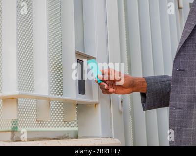 Side view of body part of crop unrecognizable African American male entrepreneur in formal suit using security access ID card for opening doorway Stock Photo