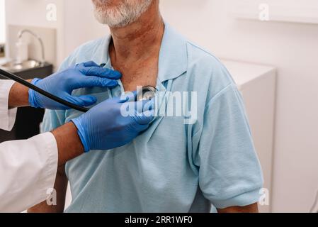 Cropped unrecognizable ethnic male doctor in gloves and medical uniform with stethoscope examining senior patient in hospital Stock Photo