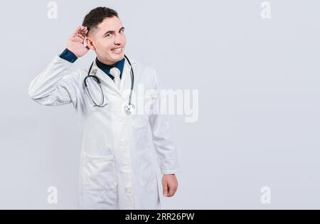 Cheerful doctor listening to a rumor. Latin doctor smiling with hand over ear isolated, Handosome doctor listening to a secret Stock Photo