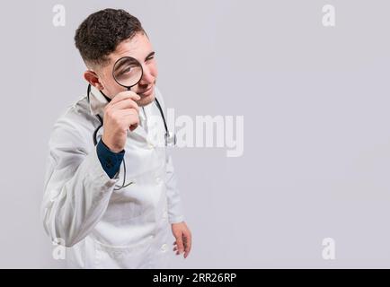 Doctor looking for something with magnifying glass looking isolated. Doctor holding magnifying glass and looking at camera on white background Stock Photo