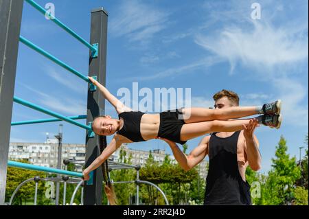 Girl doing human flag exercise with her trainer on a climbing frame. Stock Photo