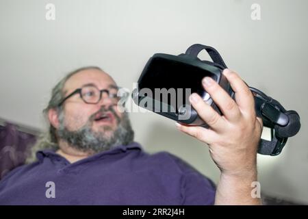 Happy Overweight man with beard and glasses amazed while holding VR on hands Stock Photo