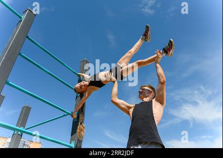 Girl doing human flag exercise with her trainer on a climbing frame. Stock Photo