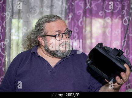 Happy Overweight man with beard and glasses amazed while holding VR on hands Stock Photo