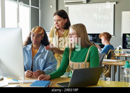 IT teacher explaining material to students on computer during lesson in the classroom Stock Photo