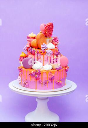 Pink, purple and orange gradient cake with cream cheese roses, macarons, cupcakes, meringues on purple plain background Stock Photo