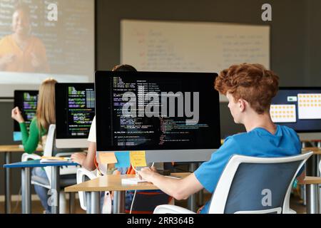 Group of students sitting at desks with computers and examining codes of software at lesson Stock Photo