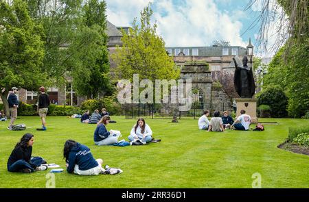 Students sitting and relaxing on grass lawn in St Mary's Quadrangle, St Andrews University, Fife, Scotland, UK Stock Photo