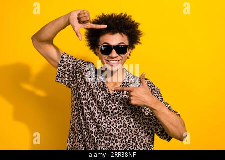 Photo of satisfied nice guy with afro hair dressed print shirt in sunglass hands focusing on smile isolated on yellow color background Stock Photo