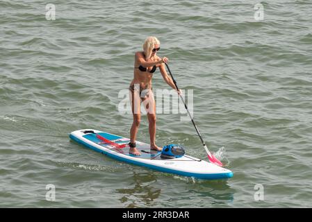 Southend on Sea, Essex, UK. 6th Sep, 2023. A hot day of the current heatwave has attracted visitors to the seaside city of Southend on Sea, with some taking to the beaches and the cool water of the Thames Estuary. Female paddle boarder wearing bikini Stock Photo