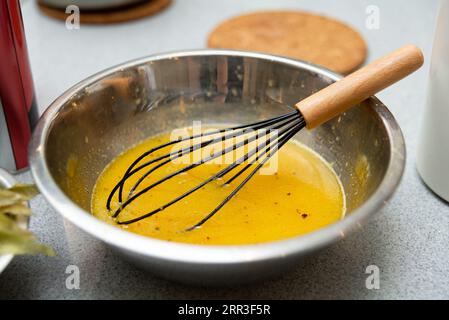 Whisking eggs with spices in a metal bowl on a kitchen counter. Stock Photo