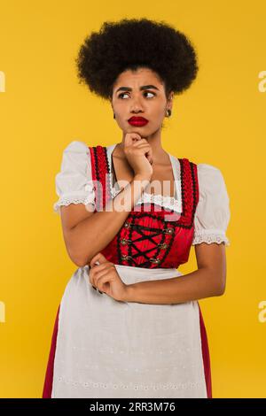 upset african american oktoberfest waitress in traditional costume looking away on yellow Stock Photo
